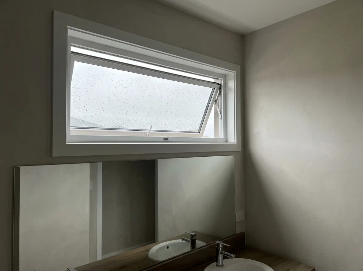 White awning window tilted open high on a bathroom wall above a vanity